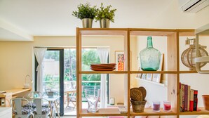 Una habitación con una estantería de madera, un comedor con sillas y una mesa, y un amplio ventanal con cortinas.