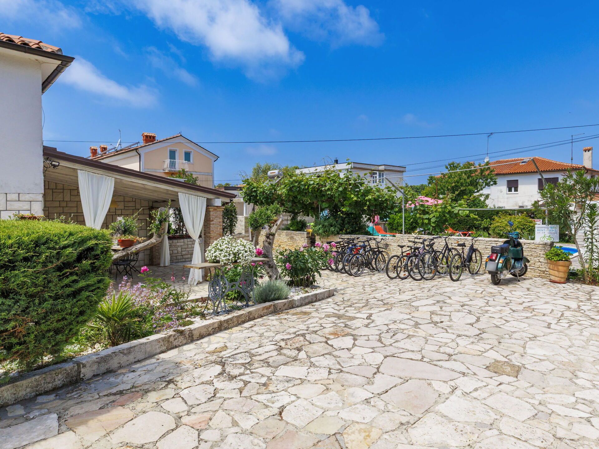 A stone-paved courtyard with a covered seating area, bicycles, and a scooter.