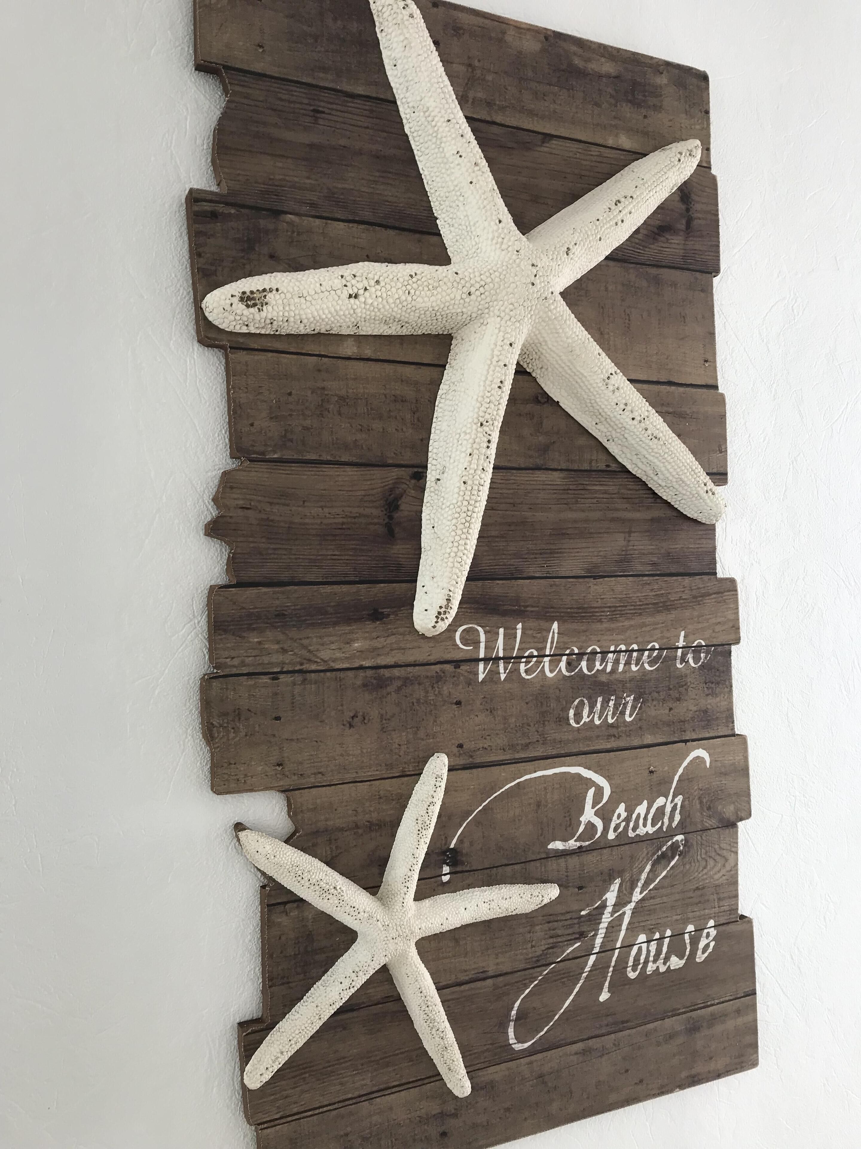 Uma placa de madeira com uma estrela-do-mar e o texto 'Welcome to our Beach House'.
