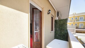 En balkong med ett vitt bord och en torkställning, en dörr med en gardin och en väggmonterad luftkonditioneringsanläggning.