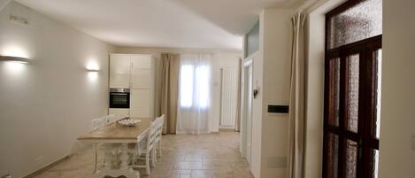 A spacious kitchen with a dining area, a large window with curtains, and a wooden door.