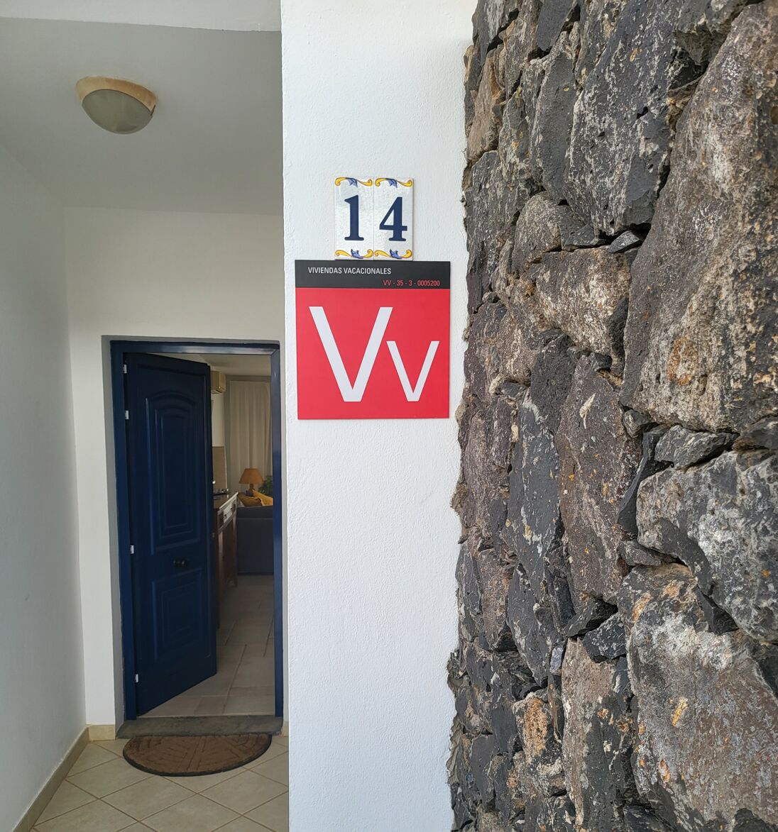 Een gang met een stenen muur, een deur en een bordje met kamer nummer 14.