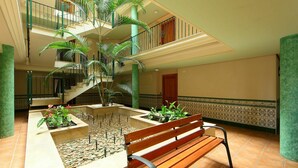 Ein mehrgeschossiges Atrium mit einem zentralen Wasserspiel, einer Holzbank und einer Treppe.