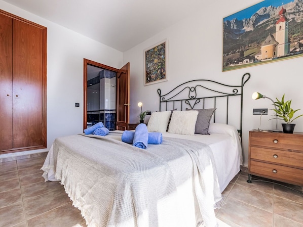 Une chambre à coucher avec un lit, une armoire en bois, un tableau, une table de chevet et une plante en pot.