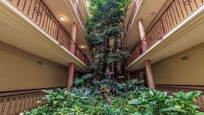Ein mehrgeschossiges Atrium mit einem vertikalen Garten in der Mitte, Balkonen mit roten Geländern und üppigem Grün am Boden.