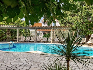 Piscina com espreguiçadeiras, pérgola e deck com ladrilho de pedra.
