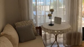 Una habitación con un sofá blanco, una mesita redonda con una computadora portátil y cortinas translúcidas.