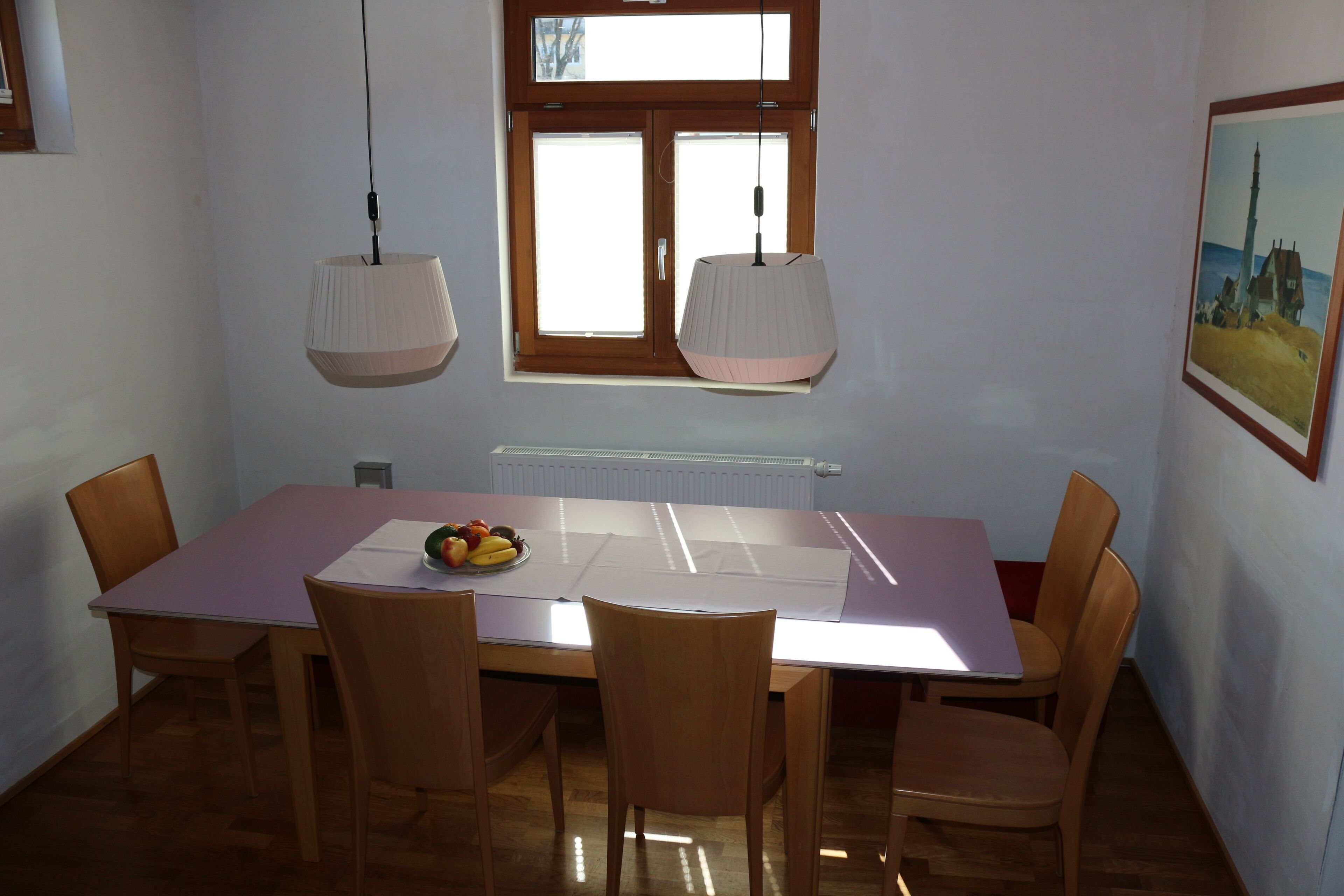 A dining area with a table, chairs, a window, and a painting on the wall.