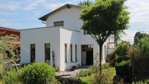 A modern white building with a flat roof, a small balcony, and a tree in front. - Central holiday home in the countryside for families with and without pets (Murnau am Staffelsee)