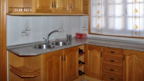 A kitchen with wooden cabinets, a stainless steel sink, and a window with a floral curtain. - B&B Apartment near Caminito del Rey (Bermejo)