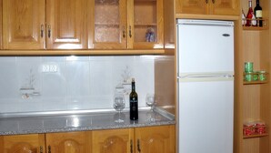 A kitchen with wooden cabinets, a white refrigerator, and a countertop with a bottle and glasses. - B&B Apartment near Caminito del Rey (Bermejo)