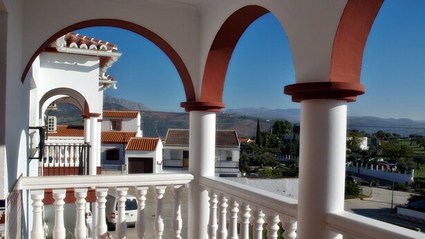 A balcony with white balustrades and red arches, overlooking a town with terracotta-roofed buildings and mountains in the distance. - B&B Apartment near Caminito del Rey (Bermejo)