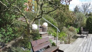 Una terraza de madera con un banco y una mesa de picnic, rodeada de abundante vegetación y árboles.