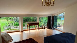 A spacious bedroom with a large window, a wooden table, a blue bed, and a red patterned rug. - Spacious semi-detached house in the east of Munich, with a view of the Alps (Markt Schwaben)
