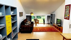A modern living room with a sofa, TV, and a dining area with a table. - Spacious semi-detached house in the east of Munich, with a view of the Alps (Markt Schwaben)