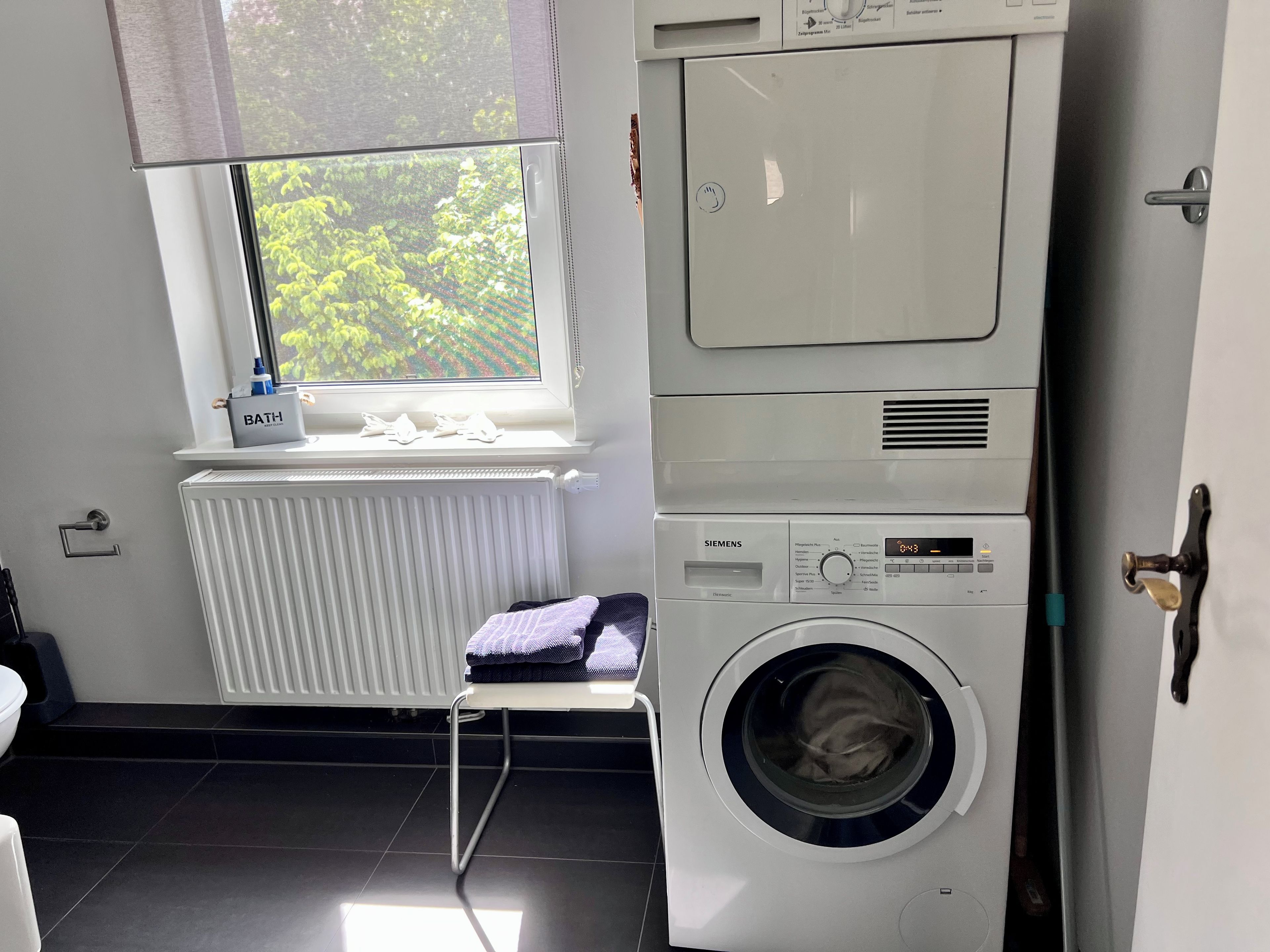 A laundry room with a front-loading washing machine, a dryer, and a radiator near a window.