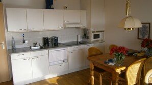 A compact kitchen with white cabinets, a microwave, a coffee maker, and a dining area with a wooden table and wicker chairs.