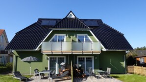 A two-story house with a green exterior, a dark tiled roof, and a balcony with glass railings.