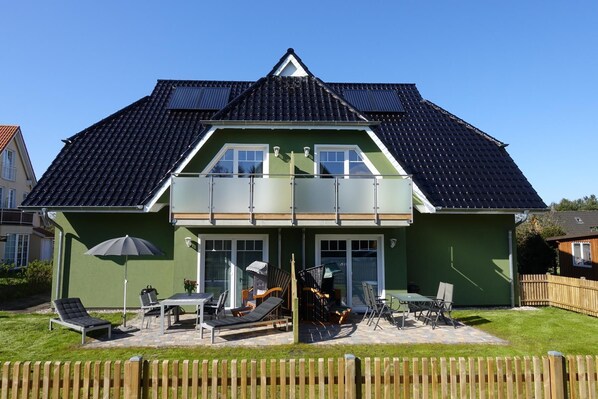 A two-story house with a green exterior, a dark tiled roof, and a balcony with glass railings.