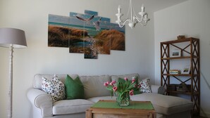 A living room with a sofa, a coffee table with a vase of flowers, a floor lamp, and a wall with a seascape painting.