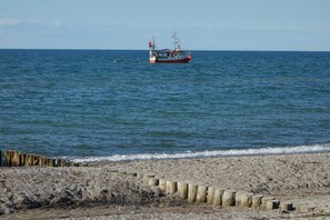 En strand med en bølgenbrekker i træ og en fiskebåd i vandet.