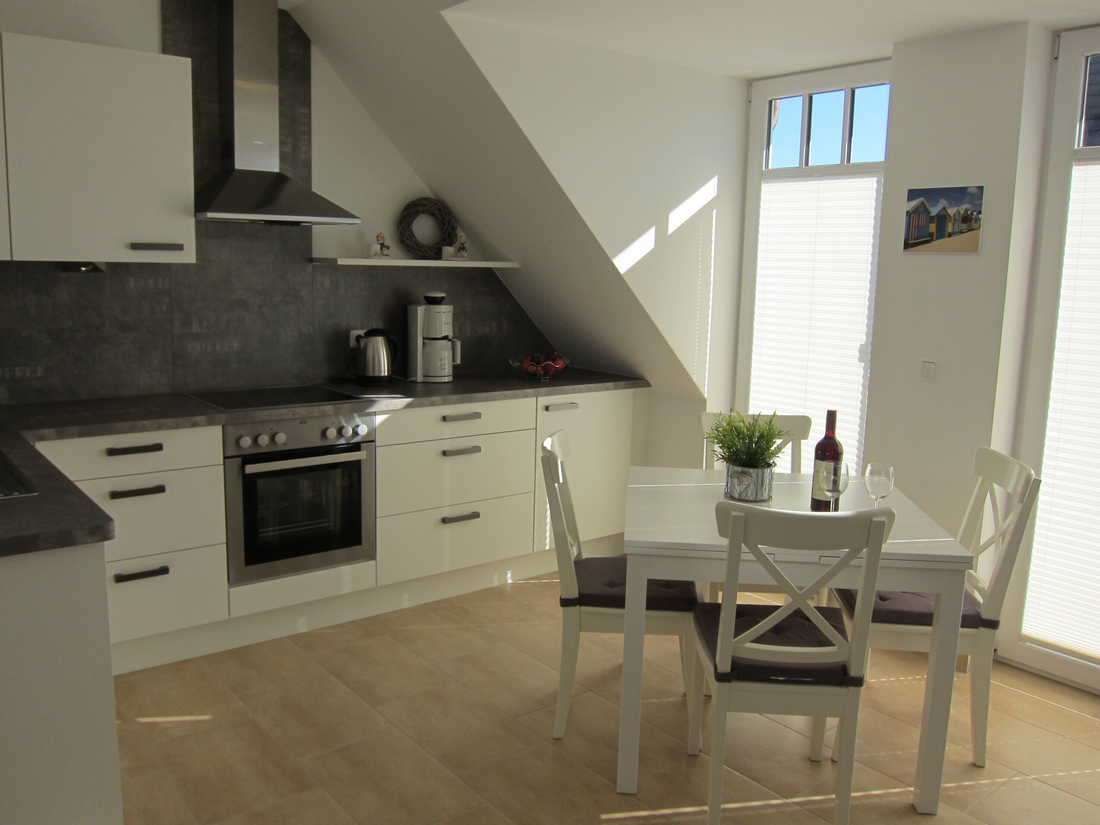 A modern kitchen with white cabinets, a built-in oven, and a dining area with a white table and chairs.