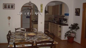 Un coin repas avec une table recouverte d’une nappe à motifs de journal, des chaises en bois et un luminaire suspendu.