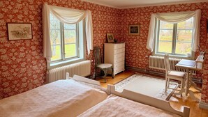 Una habitación con dos camas, un escritorio, una silla, un radiador y dos ventanas con cortinas.