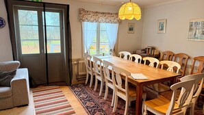 Un comedor con una mesa de madera y sillas blancas, un tapete estampado y una ventana con cortinas.