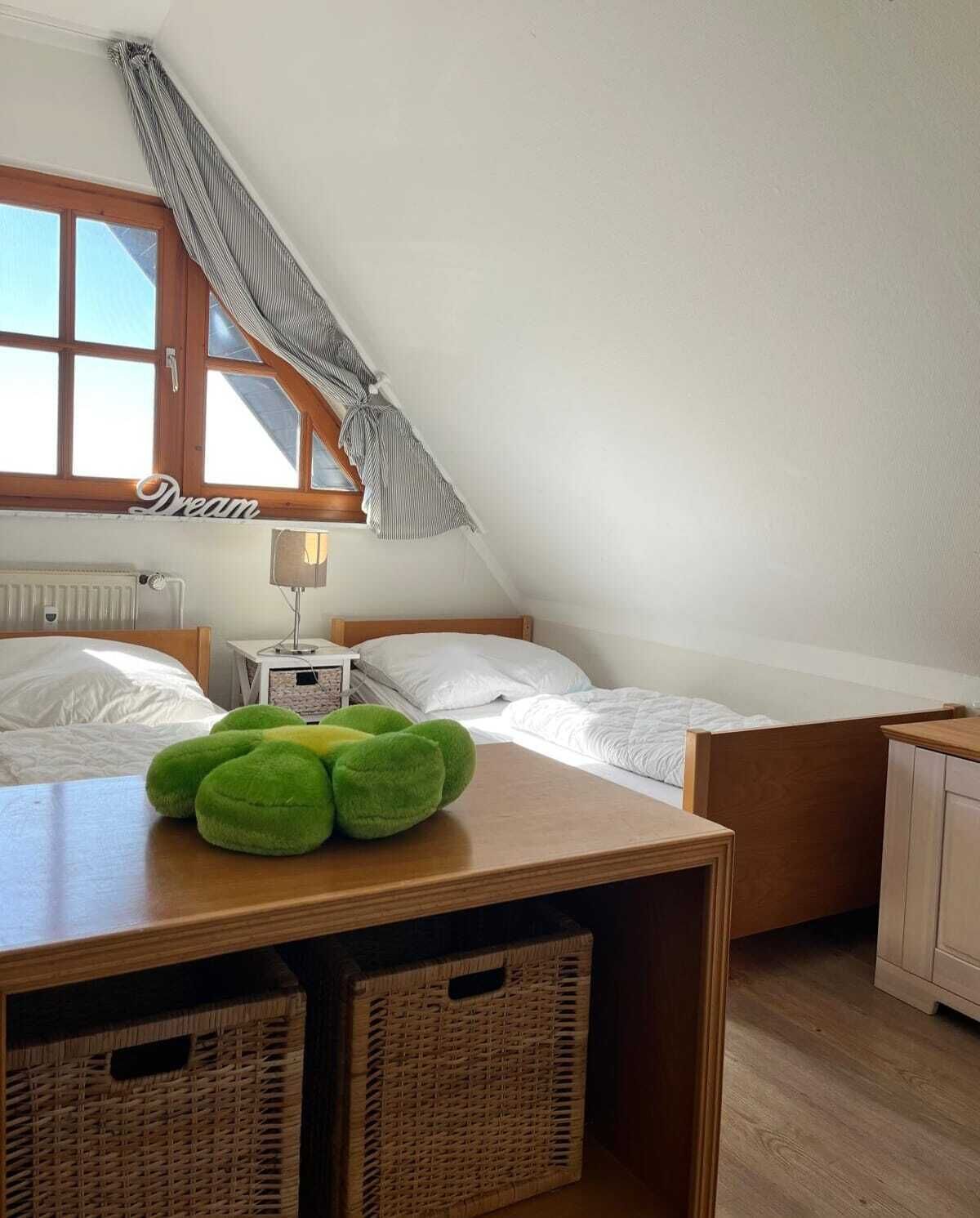 Een slaapkamer met twee bedden, een raam met gordijnen, een bedlampje en een klein tafeltje met zachte groene knuffels.