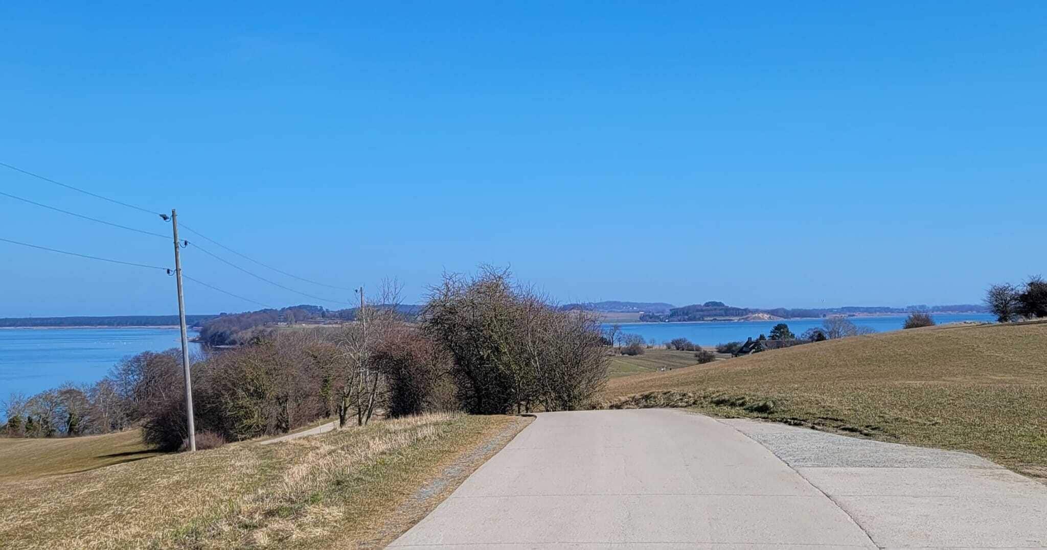 A rural road leading to a body of water with hills in the background.