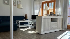 Ein modernes Wohnzimmer mit einer Couch, einem Fernseher, einem weißen Schrank und einem Fenster mit Vorhängen.