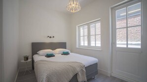 Un dormitorio con cama, mesita de noche, lámpara colgante, ventana y puerta.