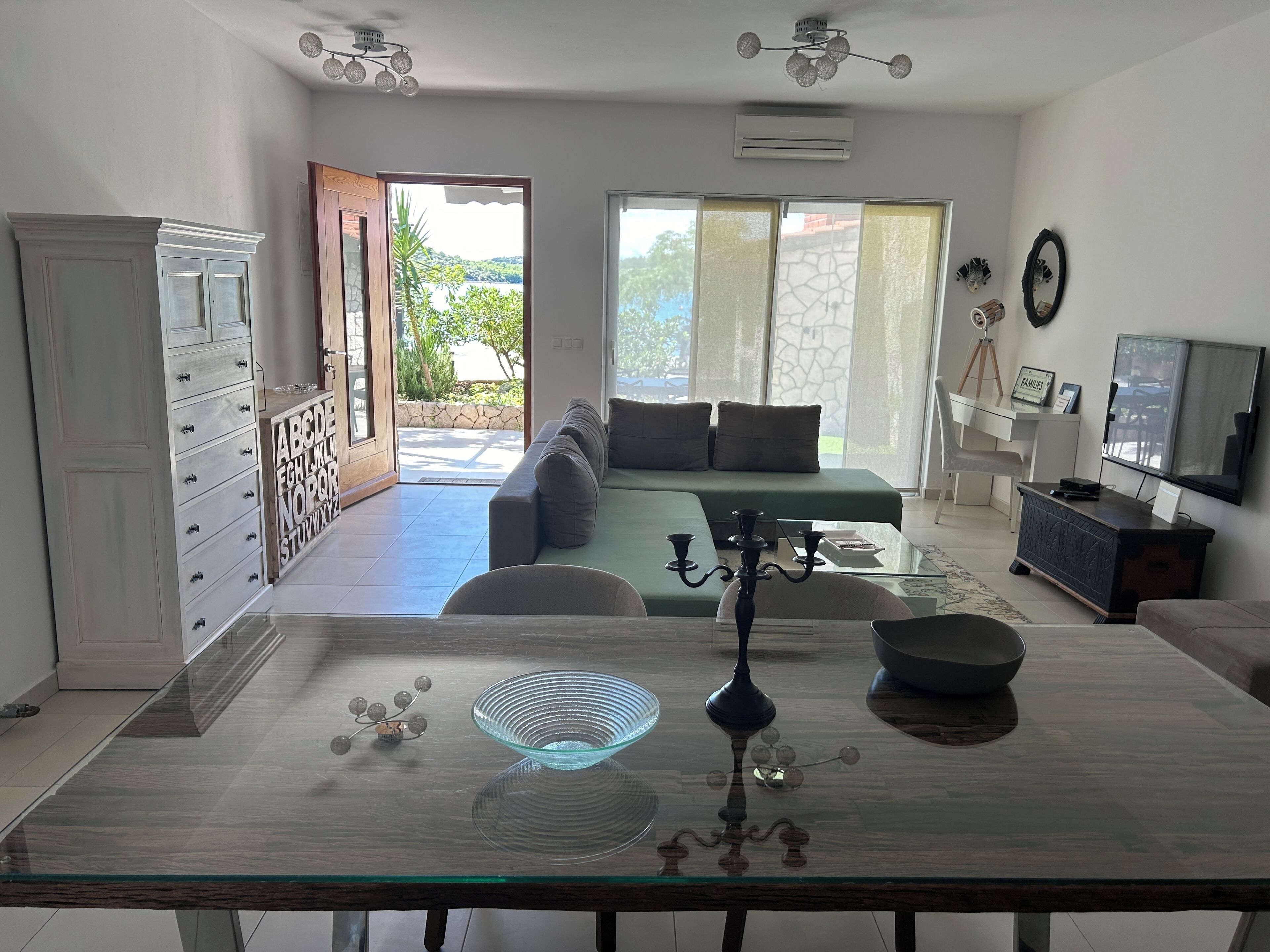 Amplia sala de estar con mesa de vidrio, sofá, televisor y vistas al exterior.
