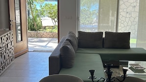 A modern living room with a sofa, a coffee table, and a view of a pool and greenery.