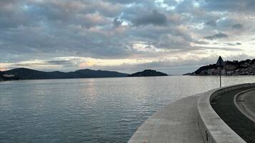 A waterfront promenade with a paved walkway and a view of the water and distant hills.
