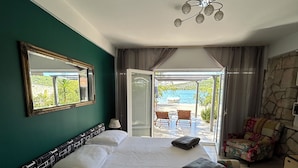 A bedroom with a large bed, a mirror, a nightstand, and a view of the outdoors.