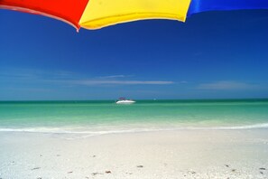 A beach with a clear blue sky, a boat in the water, and a colorful umbrella on the sand. - Beautiful Holiday House at Paradise Coast in Naples / FLorida (Naples)