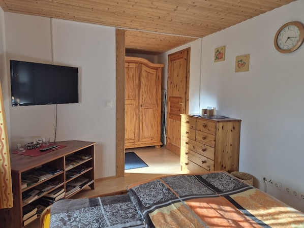 A bedroom with a bed, a TV, wooden furniture, and a clock on the wall. - Apartment i haven, Germany (Steinbergkirche)