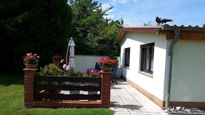 Une petite maison avec une entrée en briques, un jardin agrémenté de plantes en pot et un oiseau perché sur le toit.