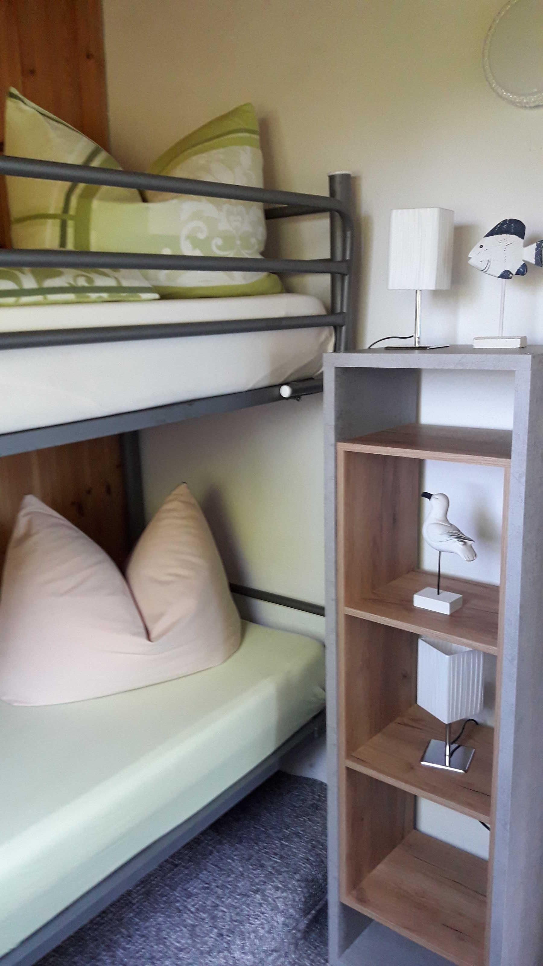 Una cama litera con almohadas, una lámpara de noche y un estante con objetos decorativos.