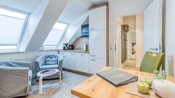 A modern loft bedroom with a sloped ceiling, skylight, and a cozy seating area with a small table and chair.