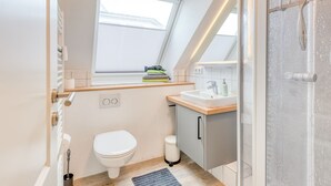 A compact, modern bathroom with a skylight, a toilet, a sink, and a shower.