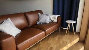 A brown leather sofa with cushions, a small round table with a stool, and a wooden floor. - Wonderful holiday house on the Nollur farm at Eyafjord (Akureyri)