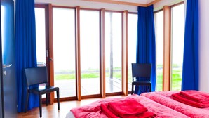 A hotel room with a large sliding glass door to the outdoors, two black chairs, a bed with red bedding, and a TV on a stand. - Wonderful holiday house on the Nollur farm at Eyafjord (Akureyri)