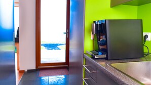 A modern kitchen with a coffee machine, a bright green wall, and a view through a door. - Wonderful holiday house on the Nollur farm at Eyafjord (Akureyri)