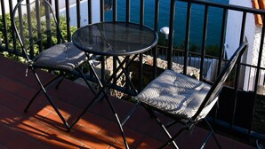 A balcony with a table and two chairs, overlooking a body of water and distant hills.