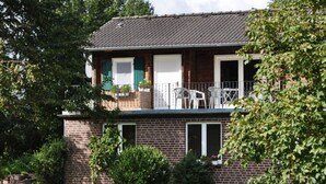 A two-story brick house with a balcony, white shutters, and a small garden area.