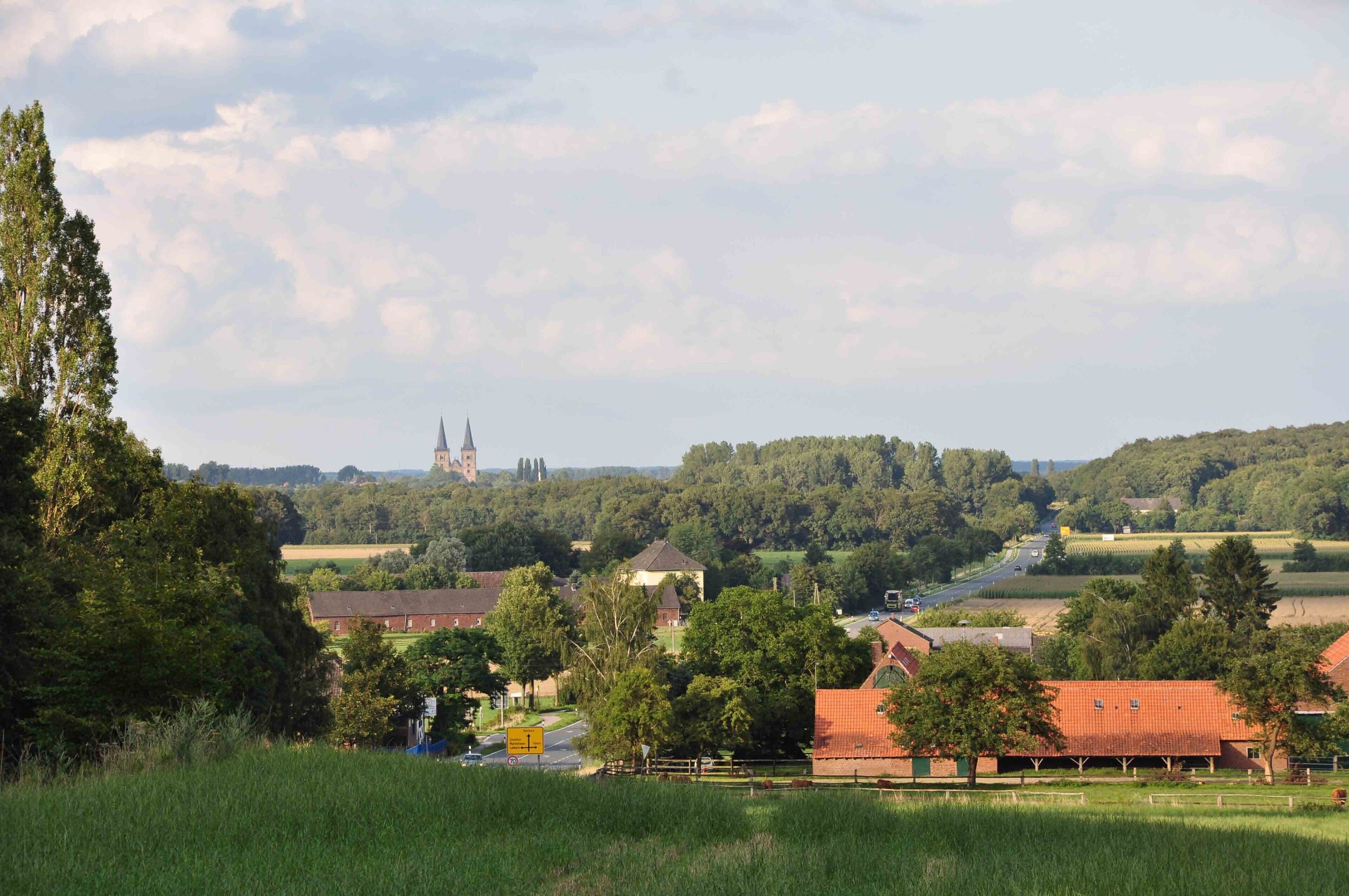A rural landscape with a church tower, houses, and fields.