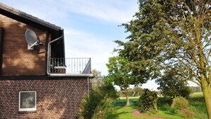 A modern building with a satellite dish, a brick wall, and a pathway leading to a green area with trees.